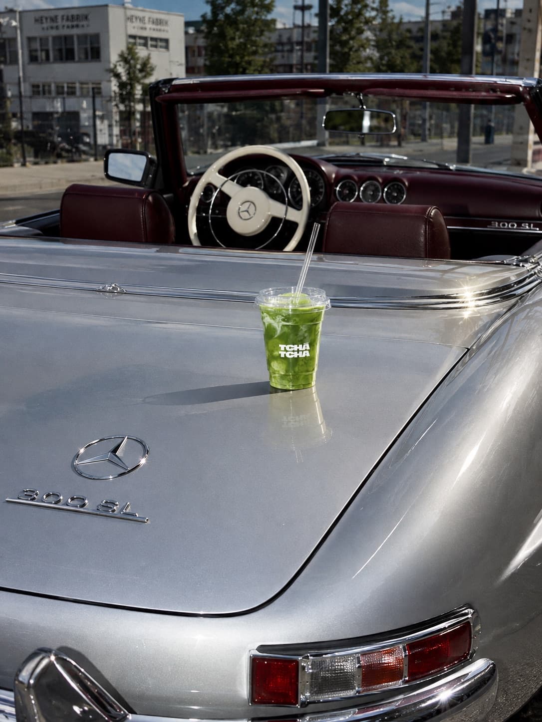 Copo de matcha gelado Tchá Tchá sobre o capô de um Mercedes 300 SL prateado