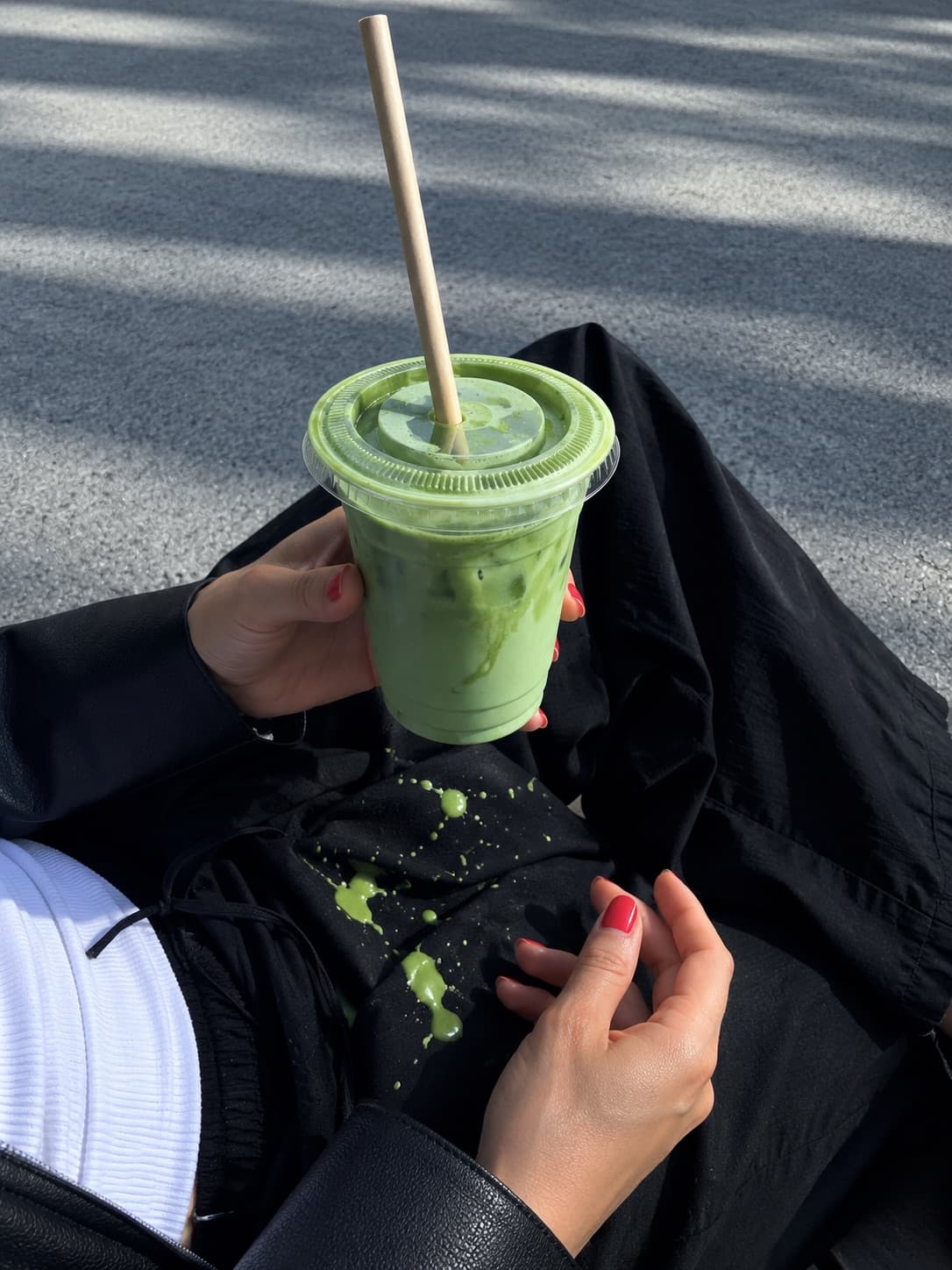 Mãos a segurar um copo de matcha gelado, com salpicos no casaco preto
